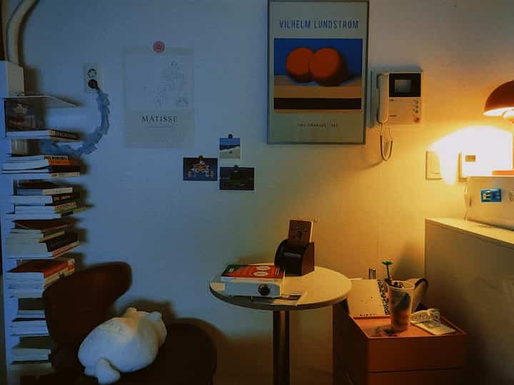 Cozy small study space in white and brown tones featuring bookshelf and sofa bed for reading.