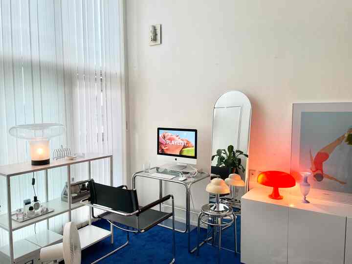 白い壁と棚、青いラグが配置されたワンルームのホームオフィス、モダンなテーブルランプと全身鏡が印象的な空間