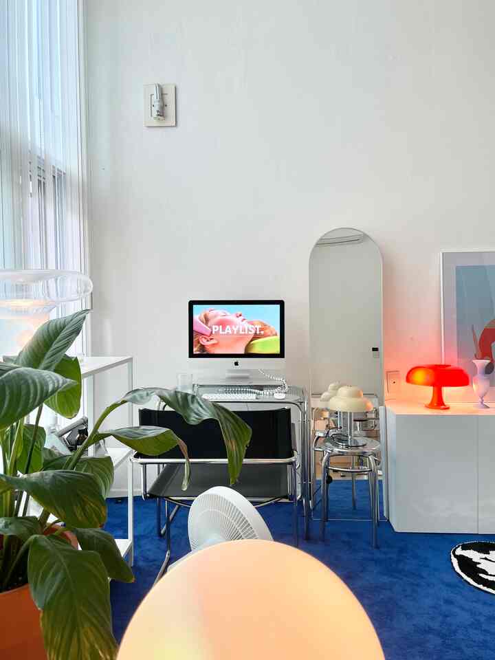 白い壁と青いラグが調和するモダンなワンルームホームオフィス、パソコンデスクと全身鏡が配置された印象的な空間