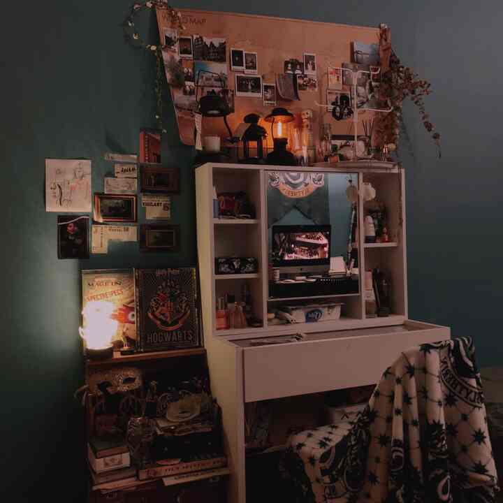 Dark green-walled walk-in closet featuring a white vanity with shelves, warm lighting, and Harry Potter-themed decor creating a cozy atmosphere
