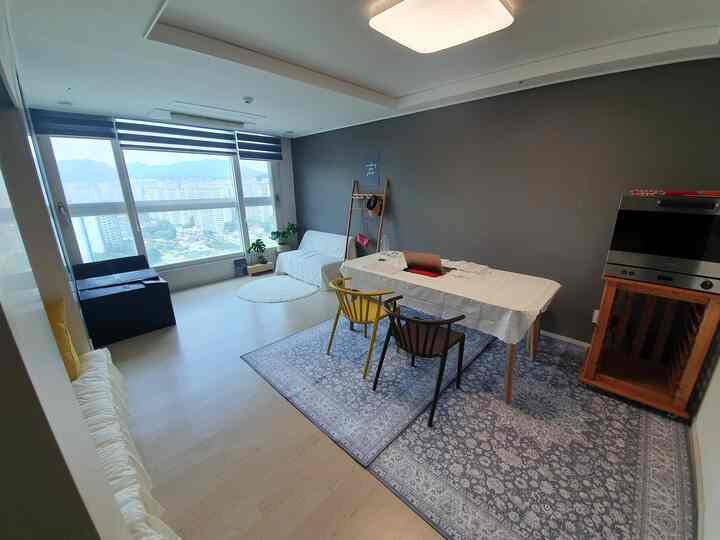 グレーの壁と白い家具が調和する1LDKリビング、ダイニングテーブルと椅子が配置されたシンプルでナチュラルな空間