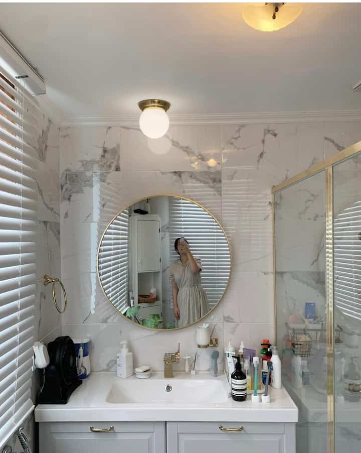 White and gold toned bathroom featuring a round mirror and sink in a clean modern setting