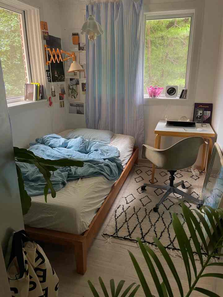 ナチュラルな木目調と白基調の小さな寝室、ベッドとデスク、オフィスチェアが配置された落ち着いた空間