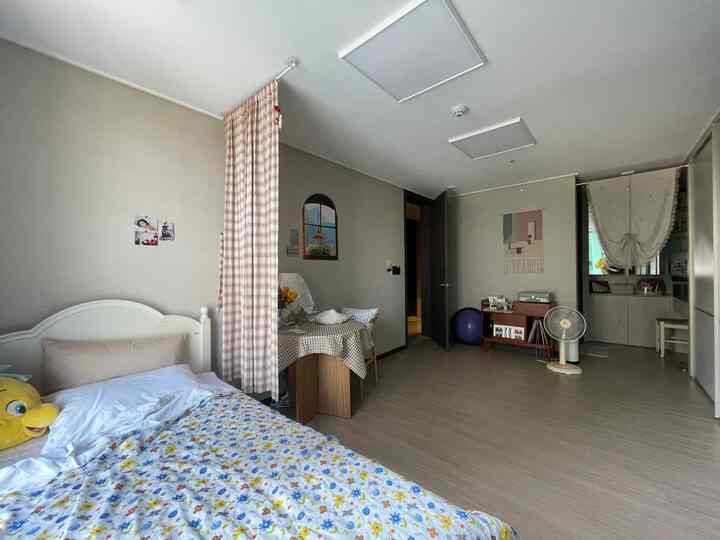 ベージュの壁と木目調の床がある子供部屋、チェック柄のカーテンと花柄の寝具が温かみのある居心地の良い空間を演出