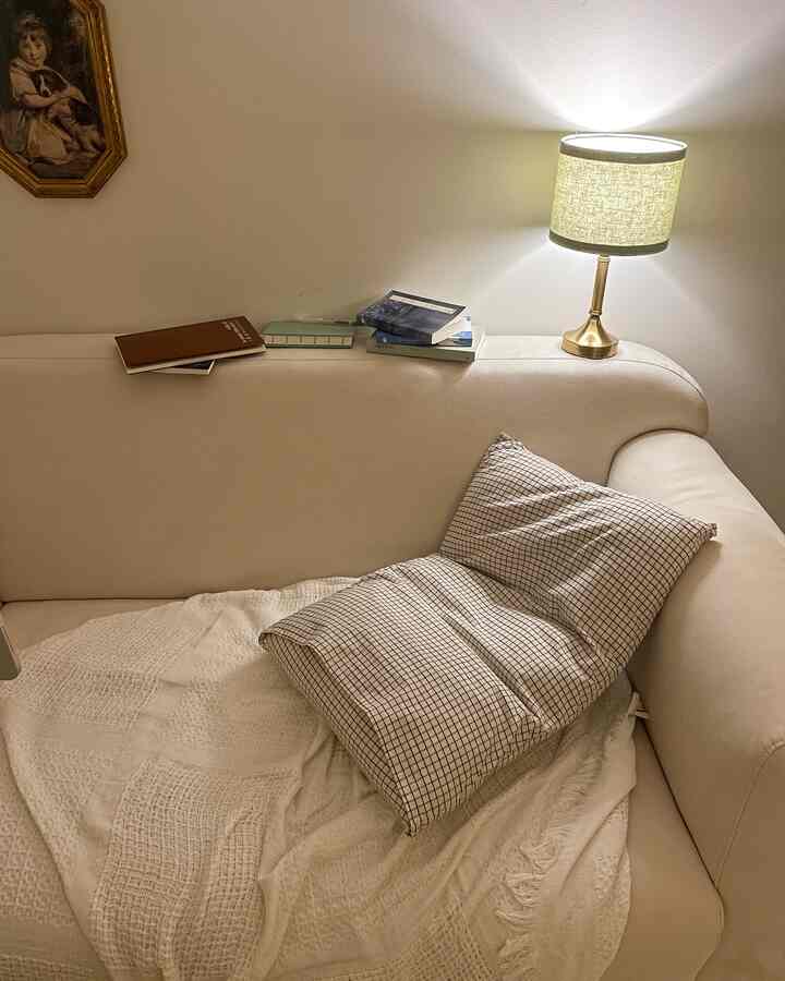 ナチュラルなベージュトーンのリビング、ベージュのソファとチェック柄の枕、テーブルランプが温かみのある雰囲気を演出するインテリア