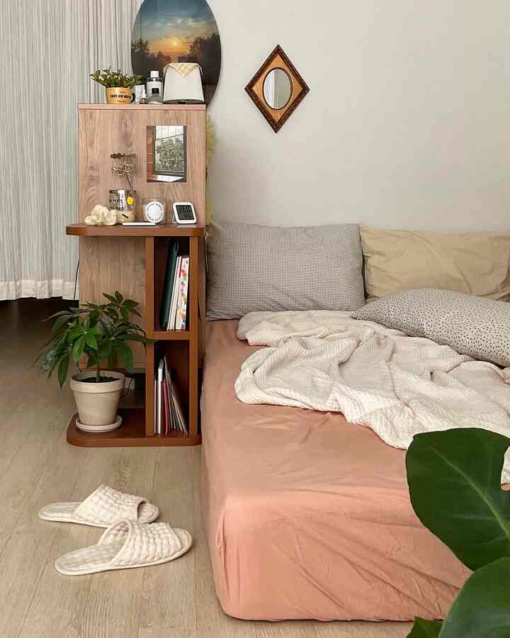 Natural tone small studio bedroom with wooden shelf and fresh pink bedding creating a cozy atmosphere