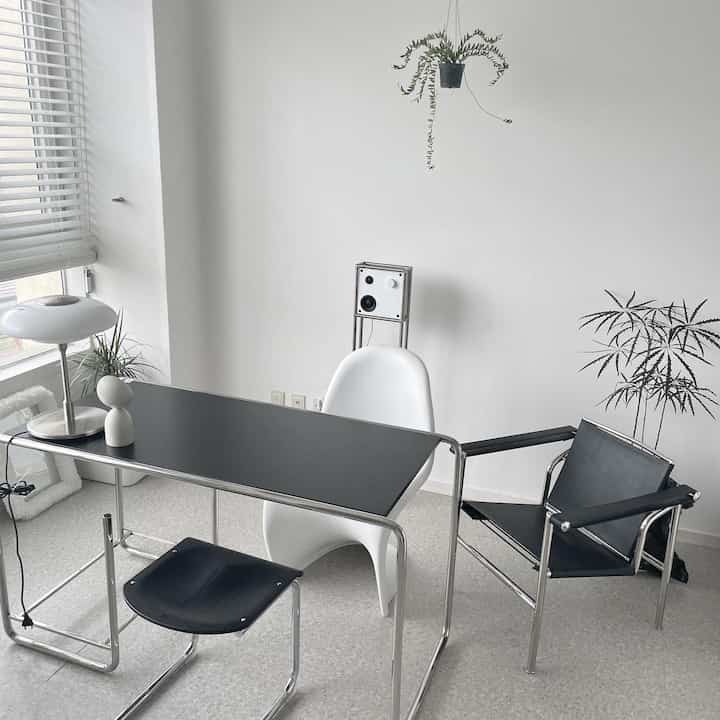 白と黒のワンルームホームオフィス、シンプルなデスクと多様な椅子が配置されたモダンで清潔感のあるインテリア