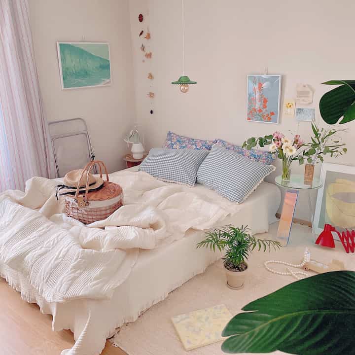 Bright white and natural toned bedroom featuring queen bed with check cushions, plants, and pendant light creating cozy atmosphere