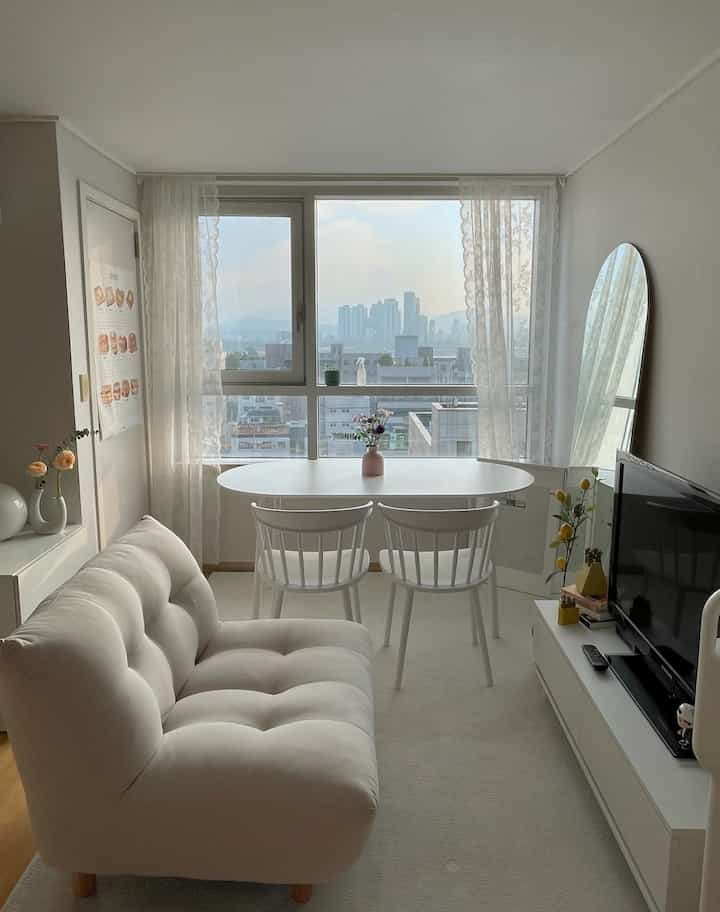 White-toned studio apartment living and dining area featuring simple furniture and large window with a cozy atmosphere