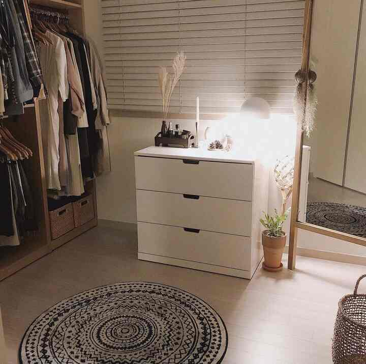 ベージュとアイボリーのナチュラルトーンのウォークインクローゼット、白いドレッサーと円形ラグ、全身鏡が配置された雰囲気のある空間