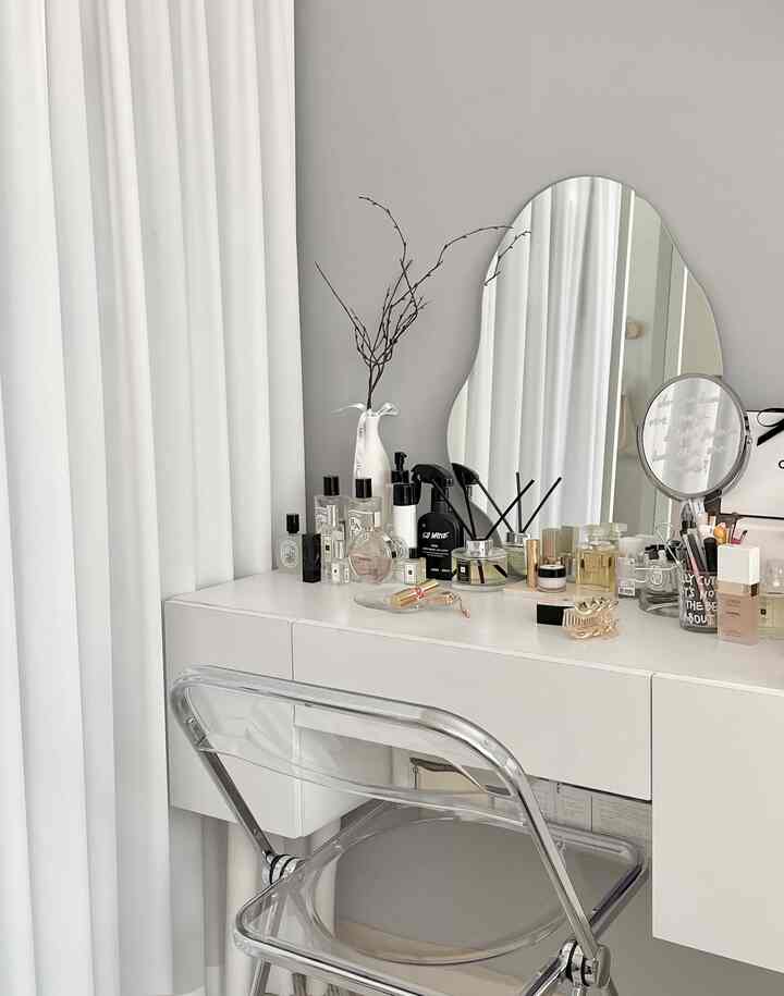 白と透明素材のミニマルな化粧台空間、透明の椅子と整然と並べられた香水ボトル