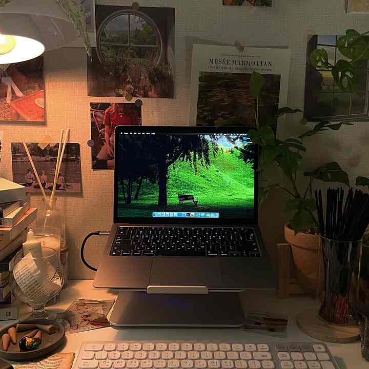 White and brown tone home office space featuring a laptop and keyboard on desk, postered wall and plant creating cozy workspace
