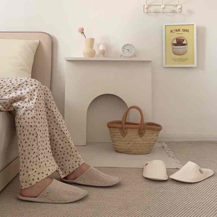 ベージュとアイボリーのトーンが特徴のワンルーム寝室、暖炉風オブジェ、ラタンバスケット、ホームカフェのポスターが配置された雰囲気のあるインテリア