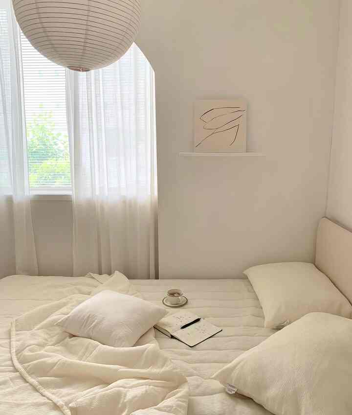 White tone bedroom featuring a low bed with white bedding and chiffon curtains, a simple and natural space