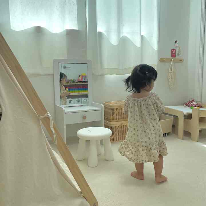 白を基調とした子供部屋、幼児用の化粧台とスツール、机、収納バスケットが配置された温かみのあるインテリア