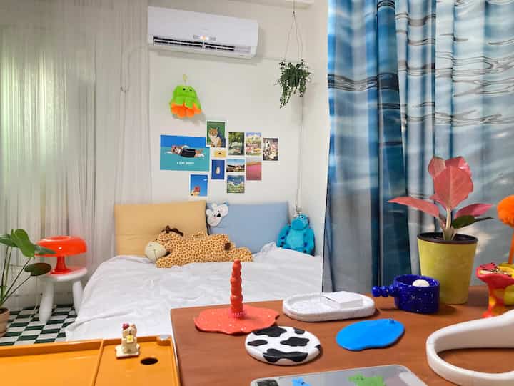 White walls and bedding with blue curtains, colorful plush toys and decorative objets in a cozy bedroom