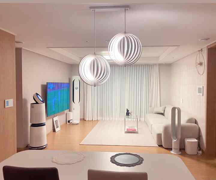 A natural modern living and dining room with white and wood tones, featuring a beige sofa and round pendant lights as focal points