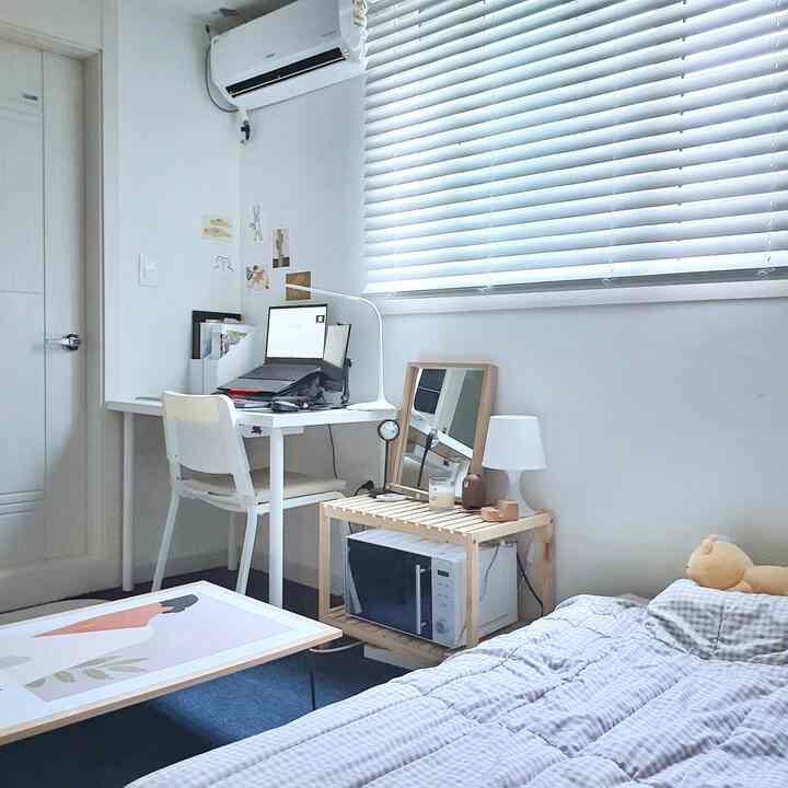A white and natural tone studio home office featuring a simple desk and bed with a minimalistic atmosphere