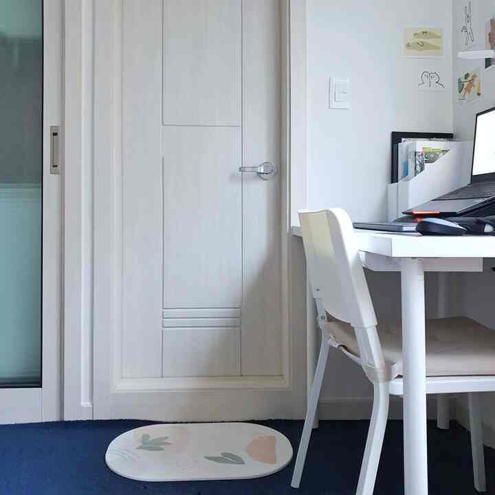 ナチュラルカラーとネイビートーンのワンルームホームオフィス、白いデスクとチェアが配置され、オフィス用ノートパソコンとポイントのフットレストがある雰囲気のある作業空間