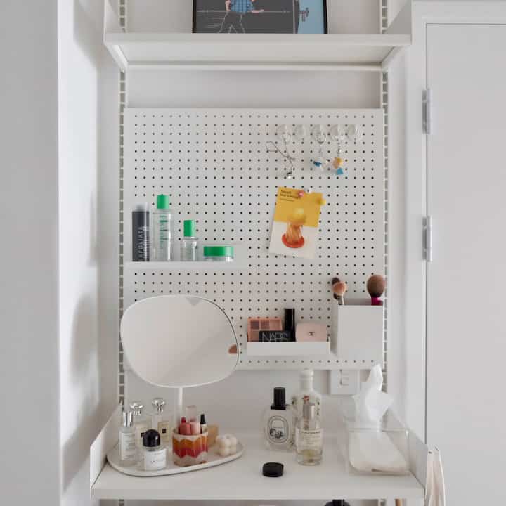 White-toned wall featuring a pegboard with shelves and a mirror, creating a simple vanity area with smart storage ideas