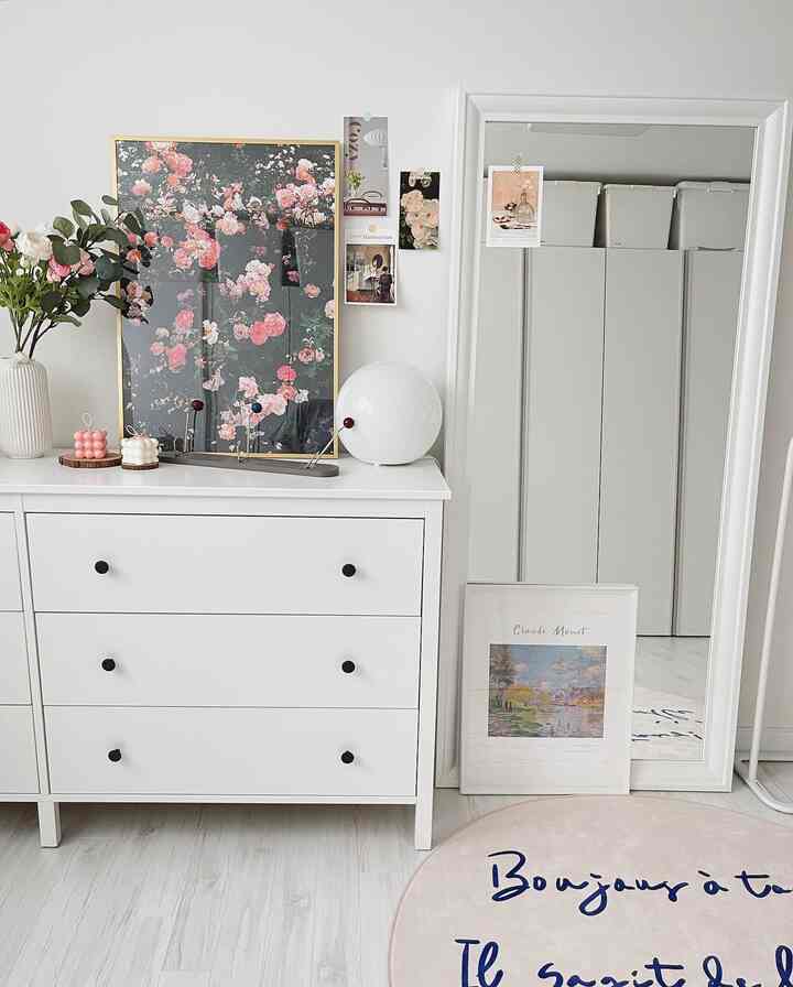 White-toned walk-in closet featuring organized chest of drawers, large full-length mirror, floral posters, and a clean natural atmosphere