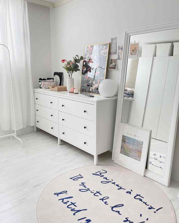 White and natural toned living room featuring a chest of drawers, full-length mirror, and decorative posters with a simple, clean atmosphere