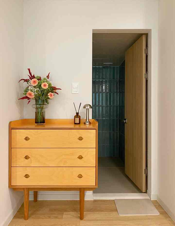 Light-toned entrance with white walls and wood-tone console table featuring a floral vase and diffuser, creating a neat atmosphere