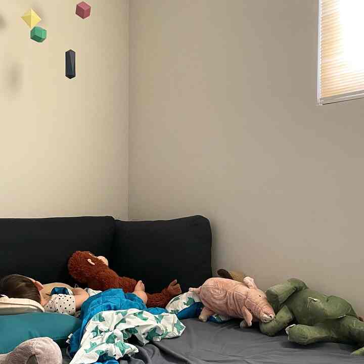 Kids' room with navy bed and polygon mobile, featuring a baby resting among stuffed animals in a calm setting