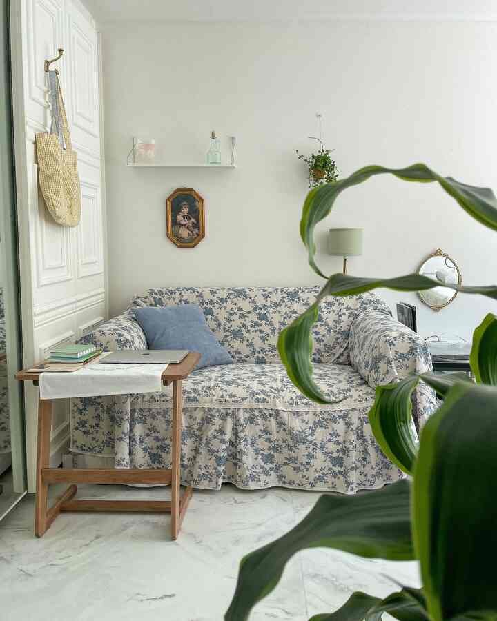 ナチュラルトーンのリビング、花柄リネンソファカバーをかけた二人掛けソファと木製サイドテーブル、ハンギングプラントが配置された落ち着いた空間