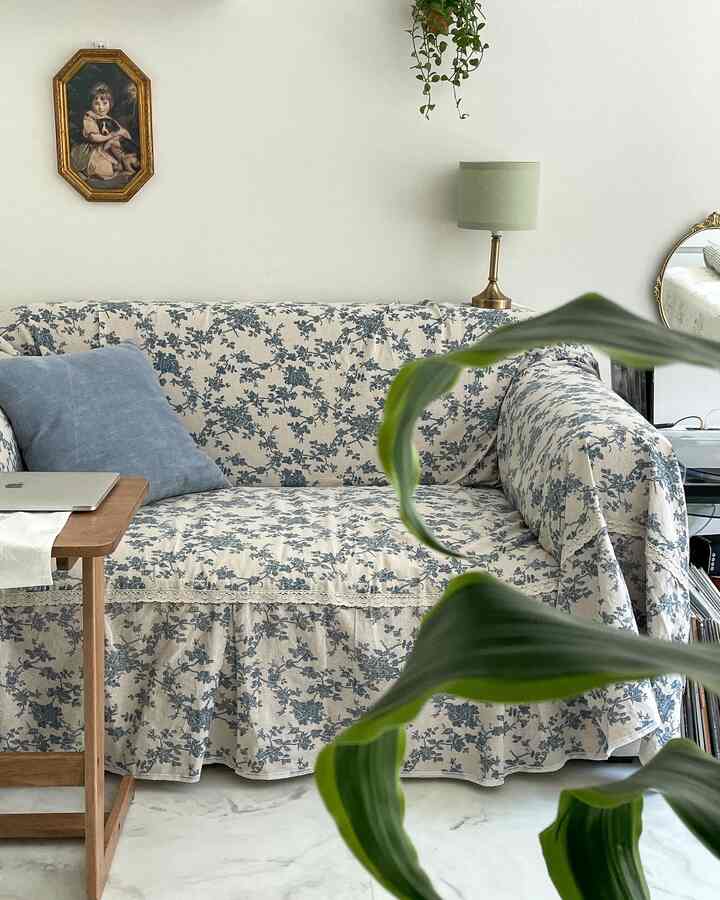 パステル調のリビングルーム、ブルーの花柄ソファカバーと木製サイドテーブルが配置された温かみのある空間