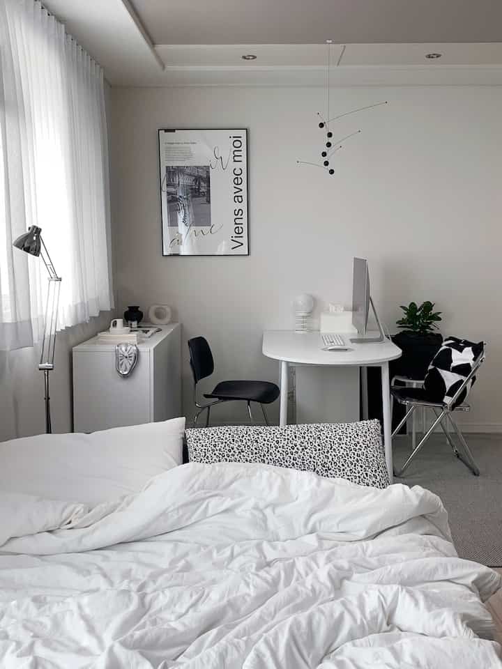 白と黒のモノトーンのワンルーム、寝具とデスク、椅子が配置されたモダンなホームオフィス空間