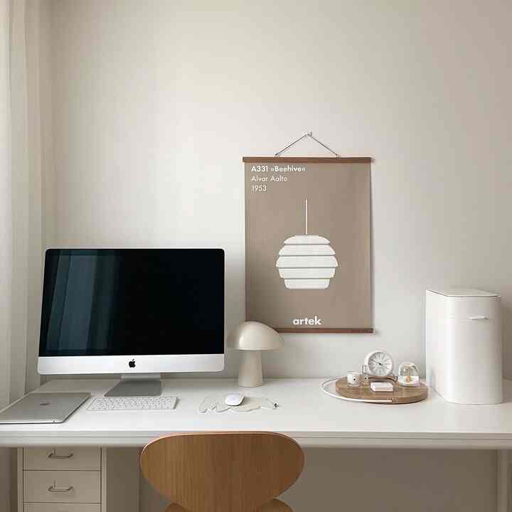 A clean home office desk space in white and wood tones featuring an iMac and simple desk lamp arrangement
