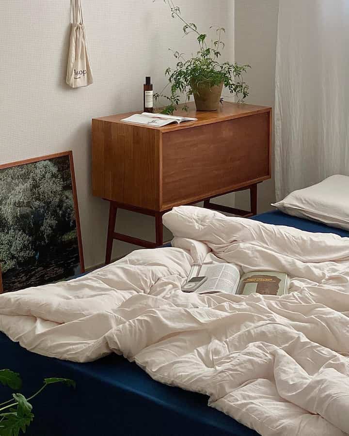 Bedroom with navy mattress and cream duvet cover, featuring a wooden cabinet and plants that create a warm natural atmosphere