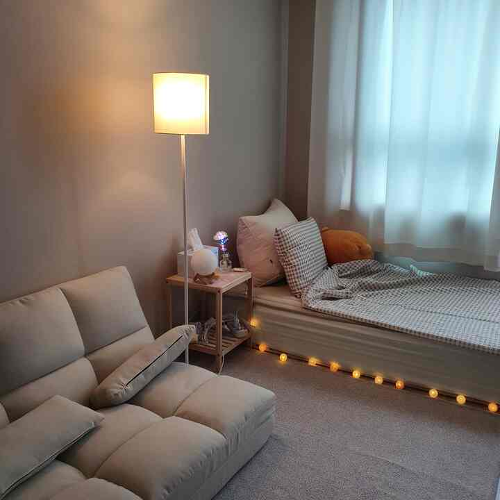 White and beige toned studio bedroom featuring sofa, bed, and floor lamp in a cozy arrangement