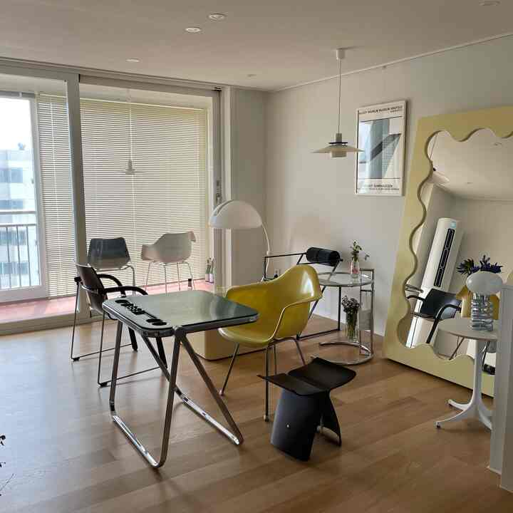 Bright natural-toned living room featuring a folding desk, yellow POLYPROP chair, and large wavy mirror in a simple modern interior