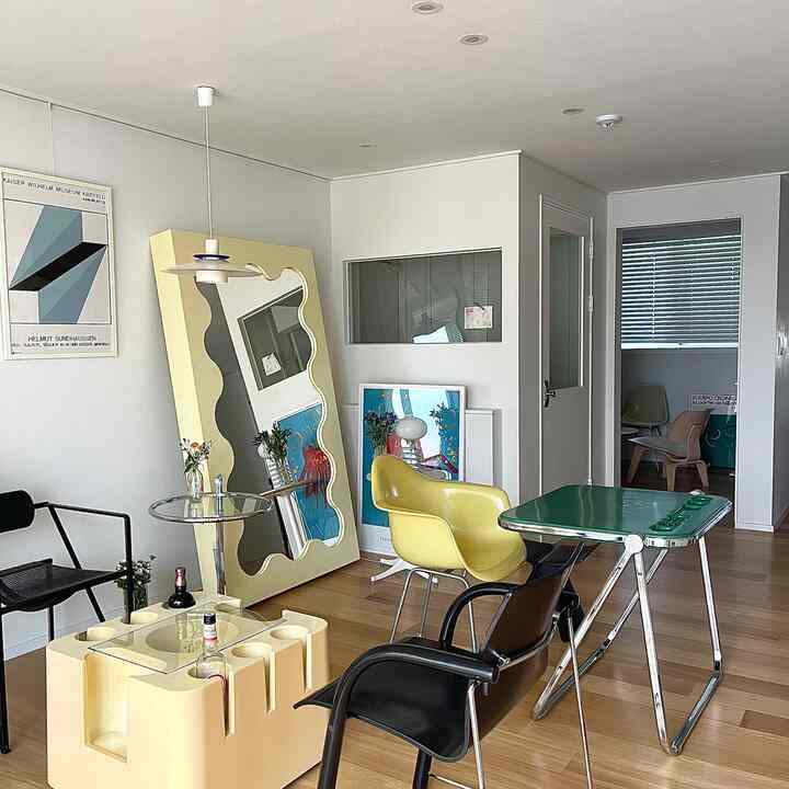 黄色と木目調のリビングルーム、アールデコスタイルの大型ミラーと複数のアームチェアが配置されたモダンなインテリア