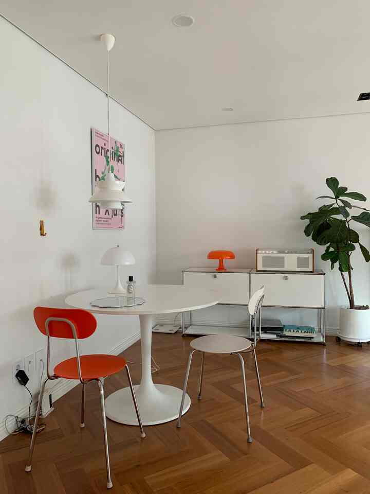 Natural modern dining space with white walls and brown wood floor, featuring orange chairs and table lamp as focal points in a clean layout
