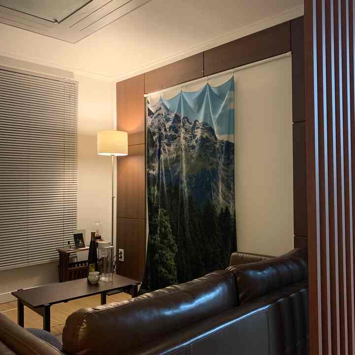 Warm wood tones and a dark brown leather sofa in a living room, featuring a mountain-print curtain and ambient floor lamp