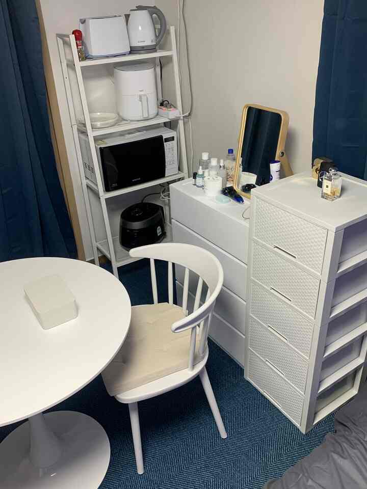 白を基調とした狭い部屋、化粧台の鏡とキッチン家電が配置された実用的なインテリア