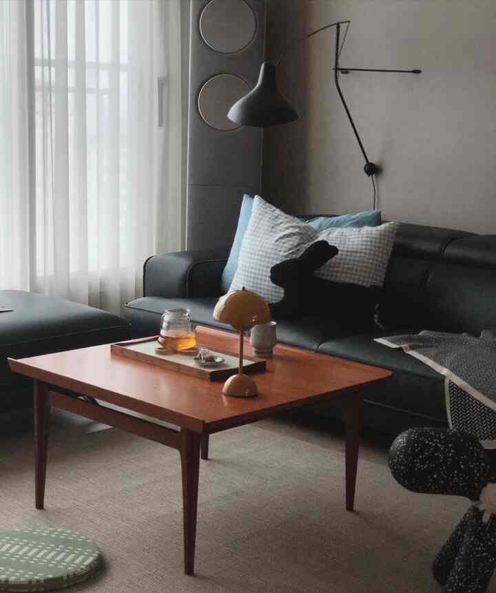 Natural modern living room featuring black sofa, wood-tone coffee table, and subtle wall sconce lighting