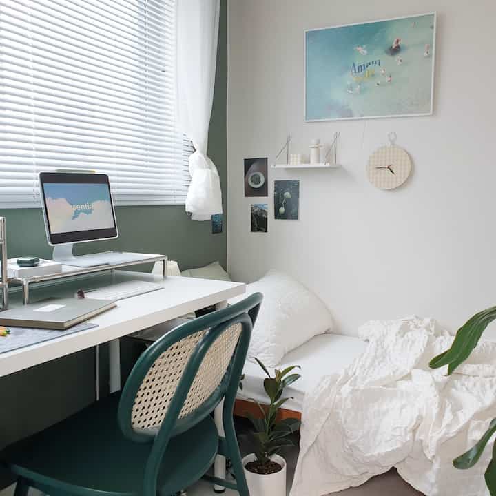 白と緑のトーンのワンルーム寝室、ミッドセンチュリーモダンの机とアイパッドが配置された落ち着いた空間