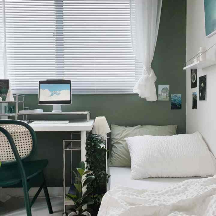 A cozy small bedroom in white and green tones featuring a desk with computer and a bed for a home office setup