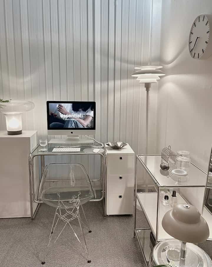 Minimal and modern small home office in white and gray tones featuring a transparent desk and drawer unit