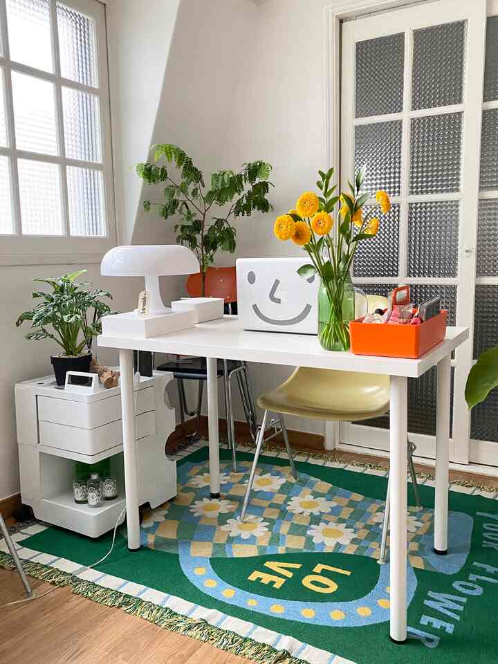 Cozy bedroom home office featuring a white table with laptop, yellow flowers, and multiple green plants