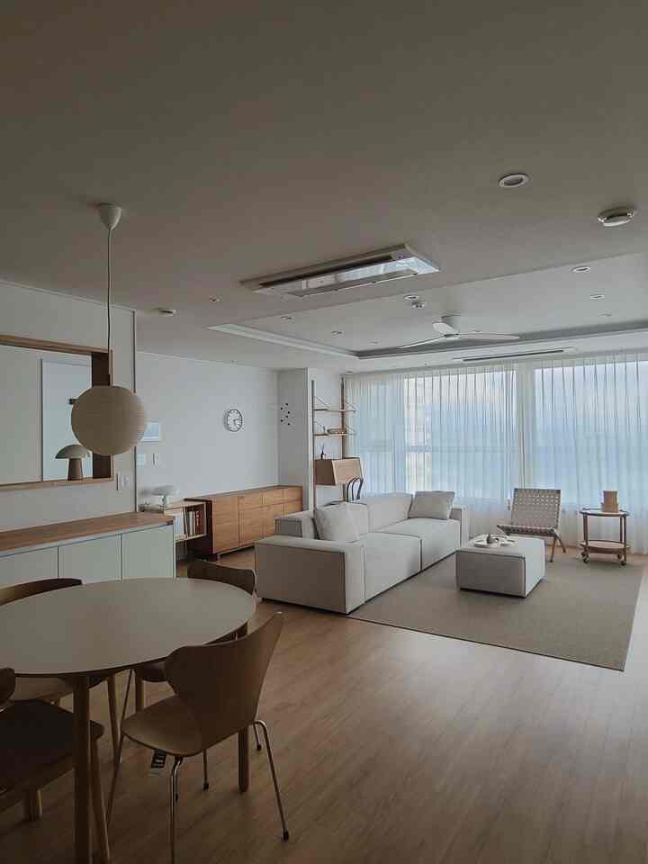 Bright white and natural wood tone living-dining combined space featuring a sofa and round dining table with a calm atmosphere