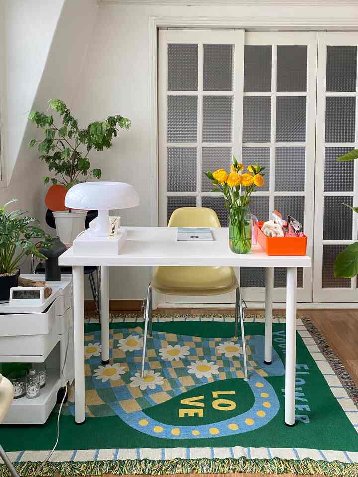 白を基調としたホームオフィス、緑の模様のラグと机の上のランプと花瓶が配置された雰囲気のあるインテリア