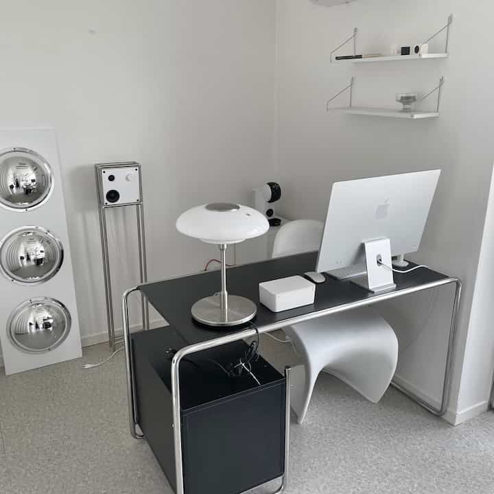 白と黒のトーンでまとめられたコンパクトなホームオフィス、モダンなデスクとAppleのiMac、シンプルな照明が配置されたミニマルなインテリア