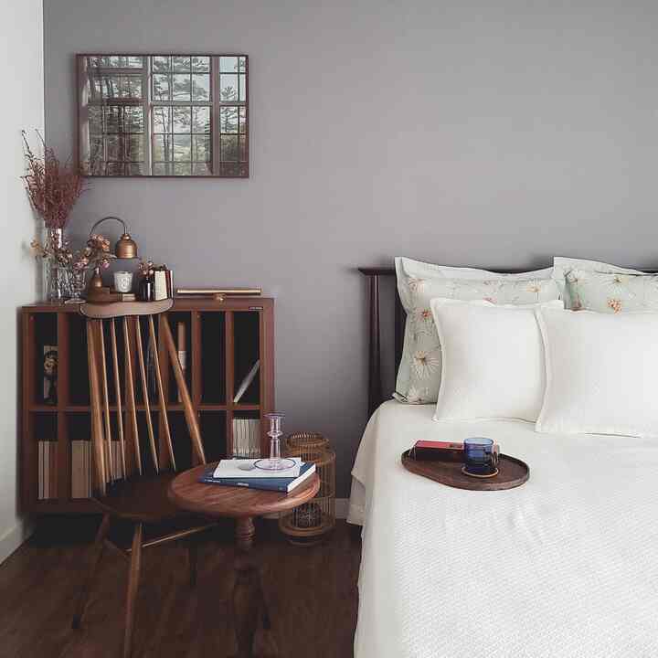 柔らかな木目調と白が調和した落ち着いた寝室、木製チェアとナイトテーブル、額縁が配されたシンプルなインテリア