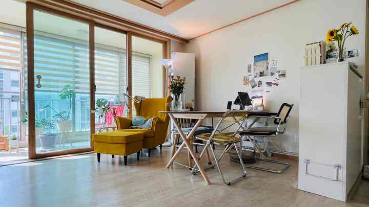 明るい木目調と白い壁のリビング、マスタードイエローのアームチェアとダイニングテーブル、フロアランプが配置されたナチュラルモダンなインテリア