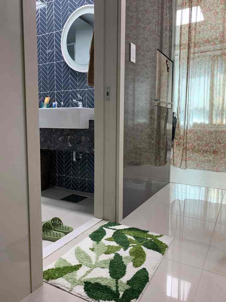 グリーン調のバスルーム入口、葉柄のバスマットと花柄のカーテンが配置された自然な雰囲気のあるインテリア